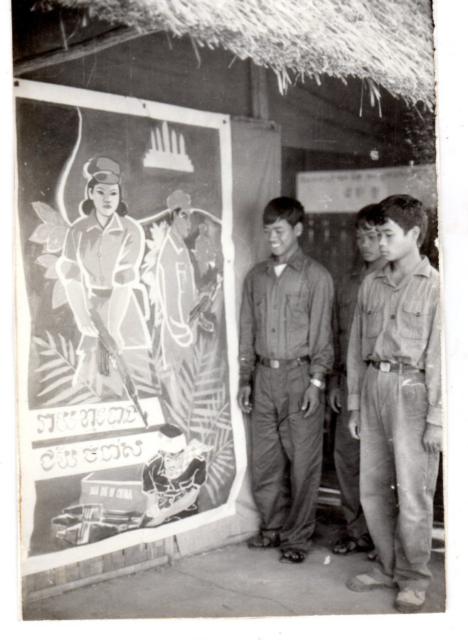 Three men stand beside a propaganda poster